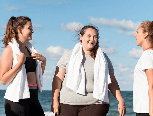Three women on the beach, wearing towels, smile and chat while enjoying the warm sun and ocean breeze.