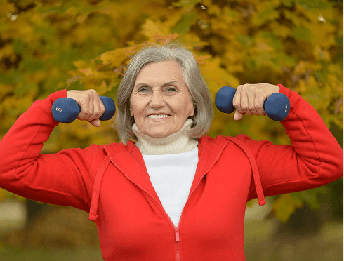 An older woman exercises with blue dumbbells, showcasing her commitment to fitness and strength training.