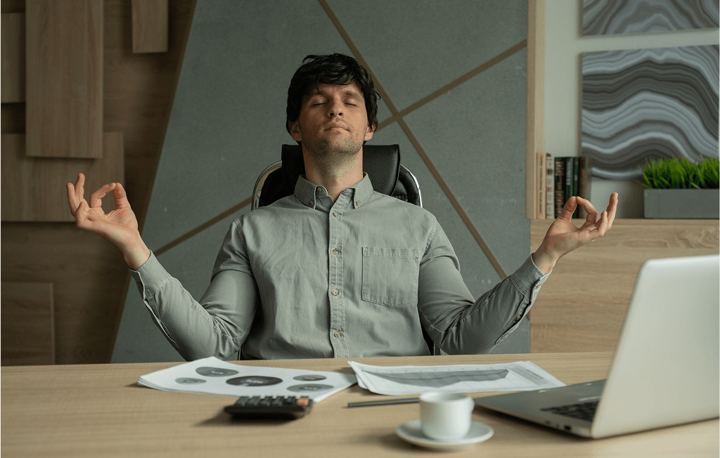 A man practices meditation in front of his laptop, creating a calm workspace atmosphere.