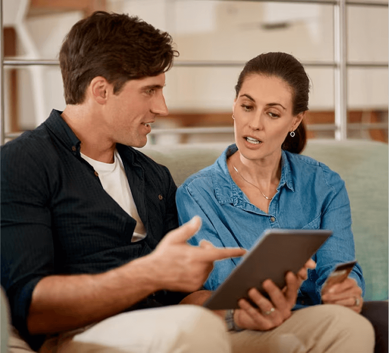 A man and woman are engaged in discussion while looking at a tablet together.