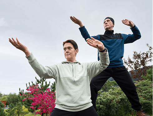 Two individuals practicing tai chi in a serene outdoor setting, demonstrating fluid movements and focus.